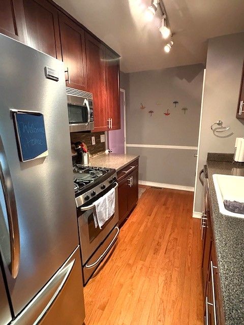 1376 Leisure Dr, Flint, MI 48507 - kitchen with stainless steel appliances, track lighting, light wood-type flooring, a sink, and dark stone countertops