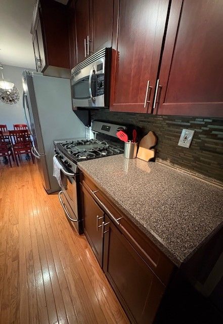 1376 Leisure Dr, Flint, MI 48507 - kitchen with stainless steel appliances, light wood finished floors, backsplash, stone countertops, and a chandelier