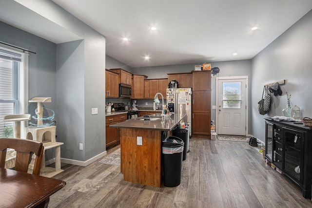 737 Bates St SE, Grand Rapids, MI 49503 - kitchen featuring appliances with stainless steel finishes, wood finished floors, brown cabinetry, a kitchen island with sink, and a sink