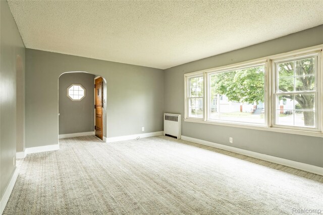 2028 9th St, Port Huron, MI 48060 - empty room with radiator, arched walkways, light colored carpet, a textured ceiling, and baseboards