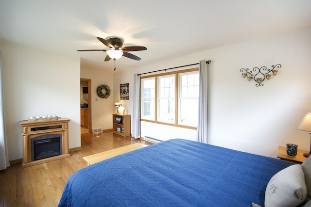 8595 E Napier Ave, Benton Harbor, MI 49022 - bedroom with a baseboard heating unit, wood finished floors, a ceiling fan, a glass covered fireplace, and baseboards