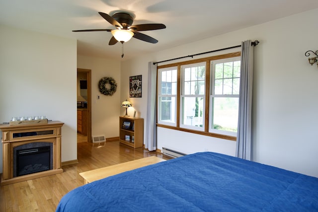 8595 E Napier Ave, Benton Harbor, MI 49022 - bedroom with a baseboard heating unit, wood finished floors, a glass covered fireplace, ceiling fan, and baseboards