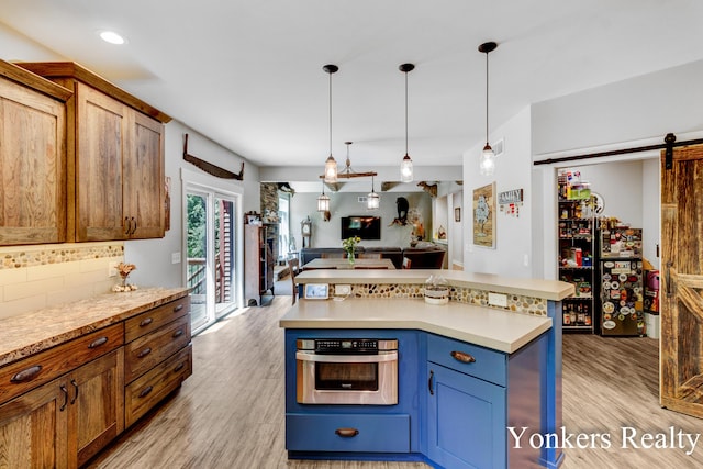 1109 Kenowa Ave SW, Byron Center, MI 49315 - kitchen featuring stainless steel oven, a barn door, light countertops, light wood finished floors, and hanging light fixtures