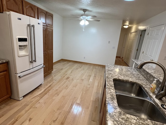 5764 W Brookwood Pl, Ludington, MI 49431 - kitchen with white refrigerator with ice dispenser, a sink, light wood-style floors, a ceiling fan, and dark stone countertops