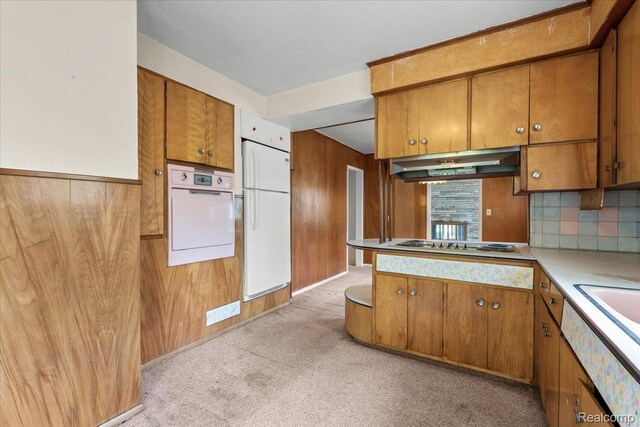 3301 S Kearsley Blvd, Flint, MI 48506 - kitchen featuring under cabinet range hood, brown cabinetry, white appliances, wooden walls, and light colored carpet