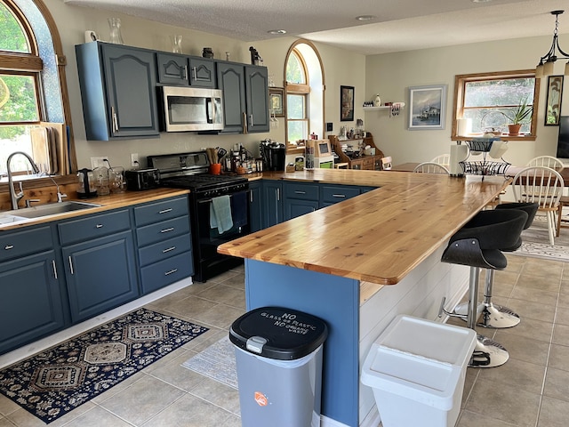 7033 N M-140, Watervliet, MI 49098 - kitchen featuring stainless steel microwave, black gas range, a sink, butcher block counters, and a kitchen breakfast bar