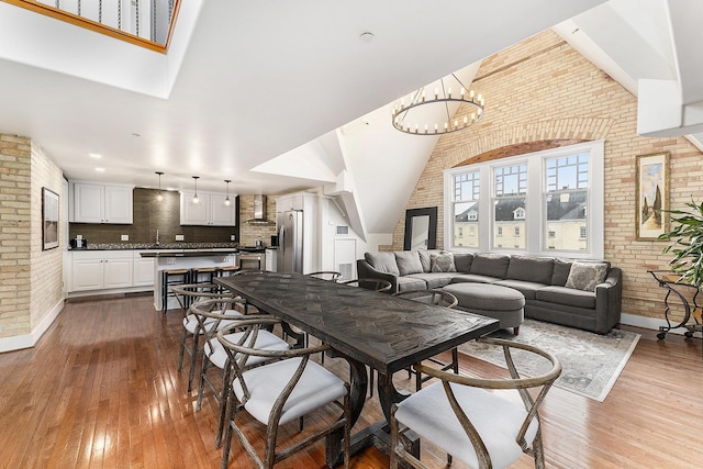810 Cottageview Dr, Traverse City, MI 49684 - dining room featuring brick wall, dark wood-style flooring, a chandelier, and baseboards