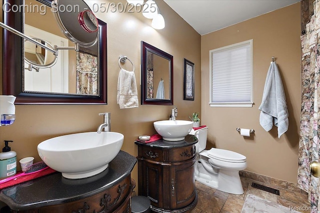 7188 Vicksburg Cir, Shelby Twp, MI 48317 - full bathroom featuring stone tile flooring, two vanities, baseboards, and toilet