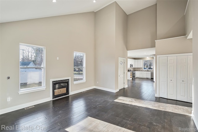527 Indian Oaks Dr, Howell, MI 48843 - unfurnished living room featuring a high ceiling, dark wood-style flooring, baseboards, a glass covered fireplace, and recessed lighting