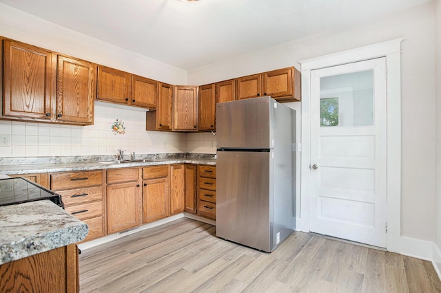 40 Eldredge St, Battle Creek, MI 49037 - kitchen featuring freestanding refrigerator, a sink, light wood-type flooring, brown cabinets, and backsplash