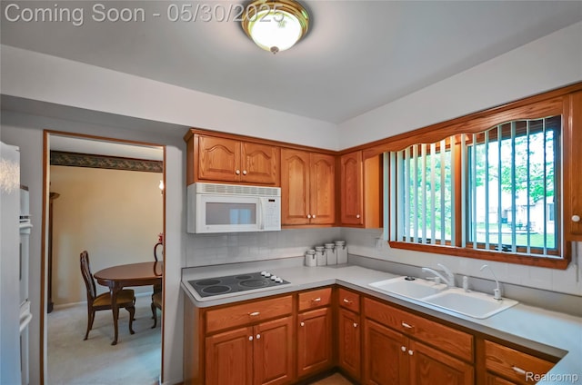 13936 Grove Park Dr, Sterling Heights, MI 48313 - kitchen with white microwave, a sink, black electric stovetop, brown cabinets, and light colored carpet