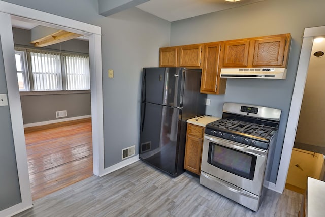 93 Illinois St, Battle Creek, MI 49014 - kitchen with gas range, under cabinet range hood, freestanding refrigerator, light wood-style floors, and brown cabinetry
