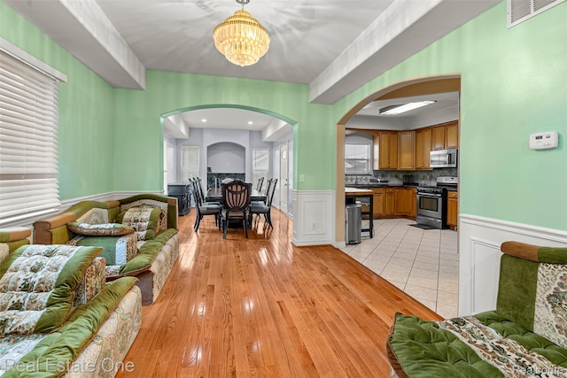 5410 Argyle St, Dearborn, MI 48126 - living room featuring arched walkways, a chandelier, a wainscoted wall, and light wood-style flooring