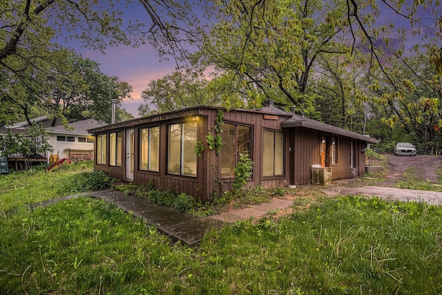 12948 Sandyside Dr, Gowen, MI 49326 - property exterior at dusk with a chimney, board and batten siding, and a sunroom