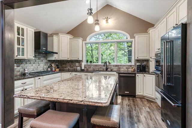 5400 Laura Dr, Shelbyville, MI 49344 - kitchen featuring stainless steel appliances, wall chimney exhaust hood, lofted ceiling, a breakfast bar, and dark stone counters