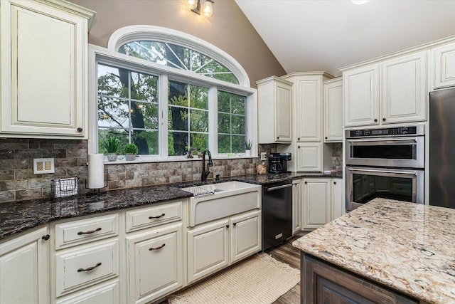 5400 Laura Dr, Shelbyville, MI 49344 - kitchen featuring vaulted ceiling, black dishwasher, stainless steel double oven, decorative backsplash, and dark stone countertops