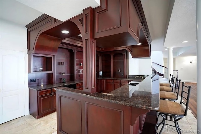 2571 N Long Lake Rd, Fenton, MI 48430 - kitchen with decorative columns, a sink, dark stone counters, a kitchen bar, and a peninsula