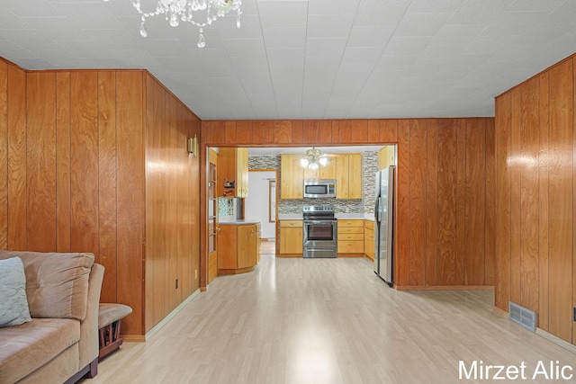 1145 Eastmont Dr SE, Grand Rapids, MI 49546 - kitchen featuring stainless steel appliances, open floor plan, light wood-style floors, brown cabinetry, and wood walls