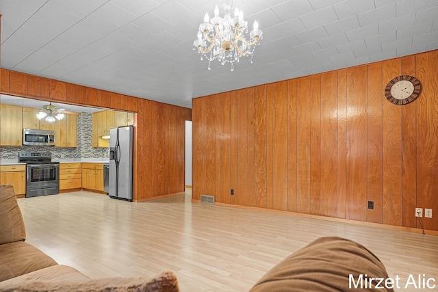 1145 Eastmont Dr SE, Grand Rapids, MI 49546 - unfurnished living room with wood walls, light wood-style flooring, a chandelier, and a ceiling fan