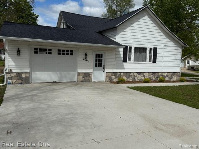 206 W 4th St, Kalkaska, MI 49646 - view of front of home with an attached garage, stone siding, and concrete driveway