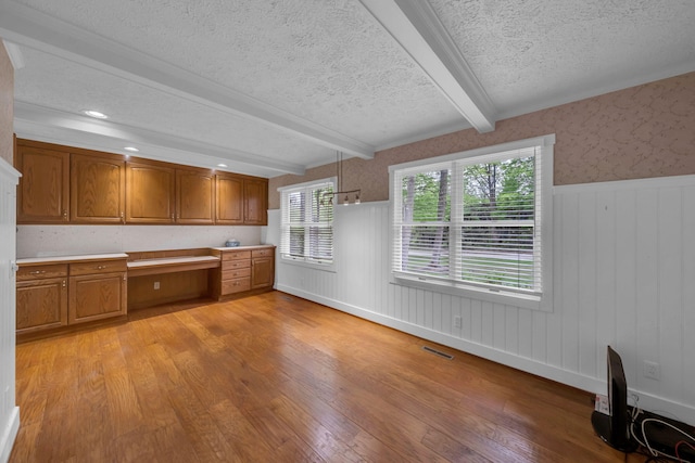 8750 20th Ave, Remus, MI 49340 - kitchen featuring beamed ceiling, a textured ceiling, light wood-style floors, brown cabinets, and a wainscoted wall