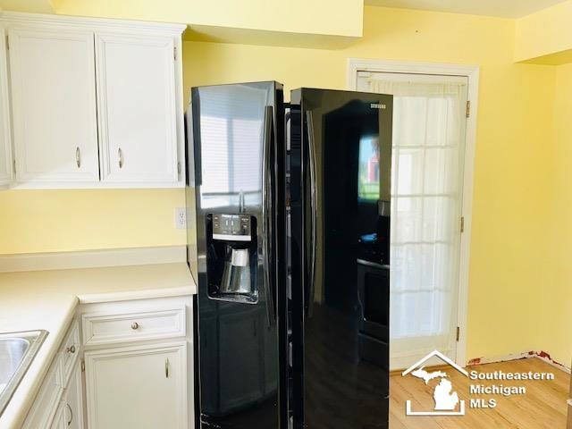 8499 Armstrong Rd, Newport, MI 48166 - kitchen featuring black fridge, white cabinetry, light countertops, a sink, and wood finished floors