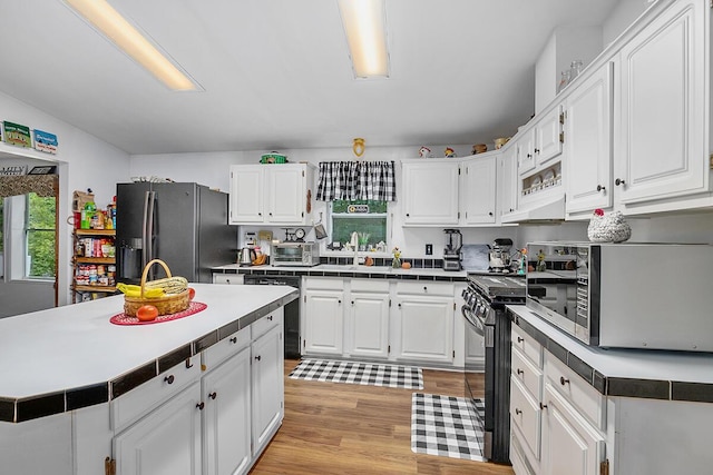 11478 E 7 Mile Rd, Tustin, MI 49688 - kitchen with black appliances, white cabinetry, light wood-type flooring, under cabinet range hood, and a sink