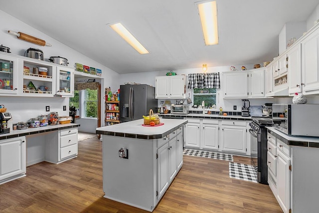 11478 E 7 Mile Rd, Tustin, MI 49688 - kitchen with black appliances, white cabinets, vaulted ceiling, light wood-style flooring, and tile counters
