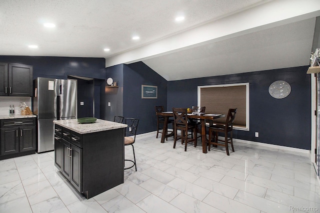 5315 Brown Rd, Millington, MI 48746 - kitchen featuring freestanding refrigerator, dark cabinetry, light marble finish flooring, a kitchen breakfast bar, and baseboards