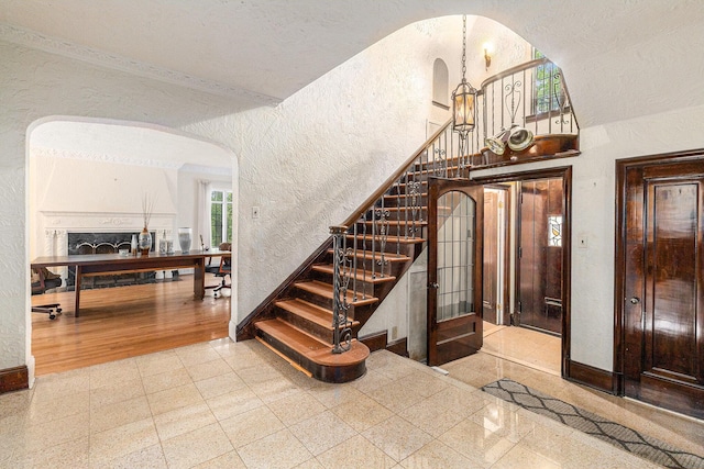 3261 Sherbourne Rd, Detroit, MI 48221 - staircase featuring a textured wall, baseboards, arched walkways, granite tiled floors, and a chandelier