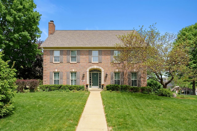 3638 Bellflower Dr, Portage, MI 49024 - colonial house featuring a chimney, a front yard, brick siding, and a shingled roof