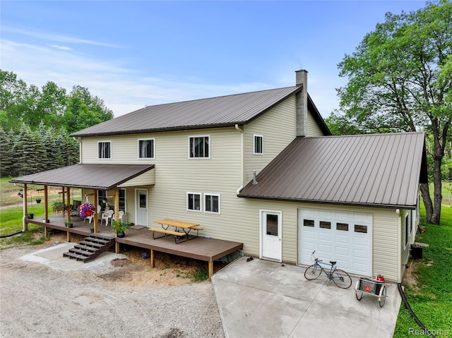 8875 N Lakola Rd, Tustin, MI 49688 - view of front of house featuring metal roof, covered porch, a garage, driveway, and a chimney