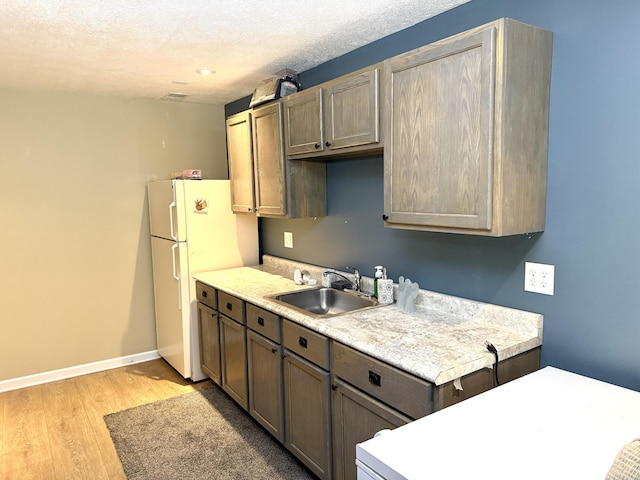 6981 Jennifer Ln, Portland, MI 48875 - kitchen with a sink, light countertops, light wood-style flooring, freestanding refrigerator, and a textured ceiling
