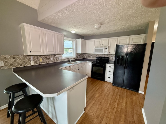 6981 Jennifer Ln, Portland, MI 48875 - kitchen featuring black appliances, a peninsula, dark countertops, a sink, and white cabinetry