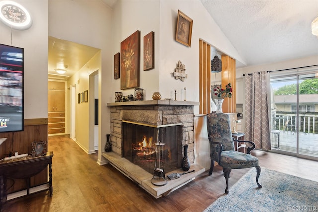 3307 Mackin Rd, Flint, MI 48504 - living area featuring vaulted ceiling, wood finished floors, a stone fireplace, a textured ceiling, and wainscoting