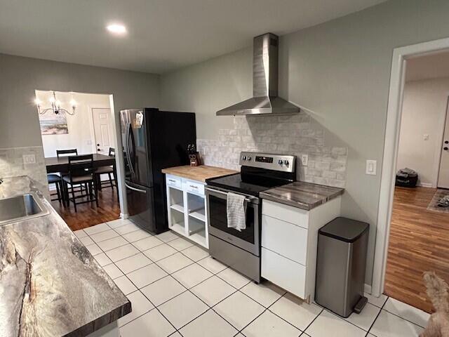 538 Monterey Dr, Benton Harbor, MI 49022 - kitchen with stainless steel range with electric cooktop, wall chimney exhaust hood, freestanding refrigerator, a chandelier, and white cabinets