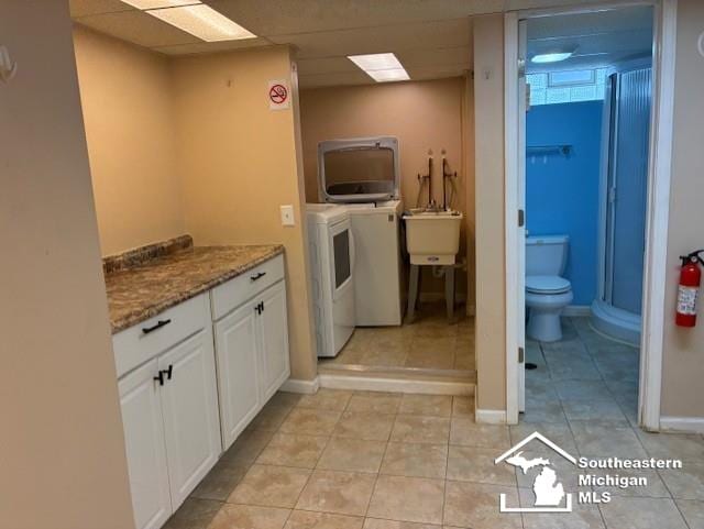 13535 Netherwood St, Southgate, MI 48195 - kitchen with washing machine and clothes dryer, light tile patterned flooring, white cabinetry, stone countertops, and a sink