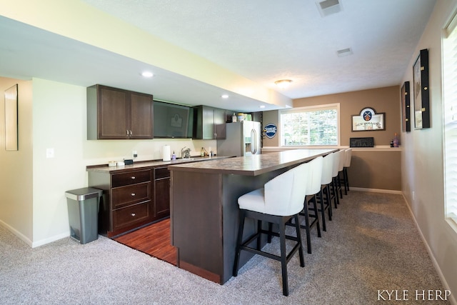 8718 Little Bend Ct, Middleville, MI 49333 - kitchen featuring stainless steel fridge, dark brown cabinetry, dark colored carpet, a kitchen bar, and recessed lighting