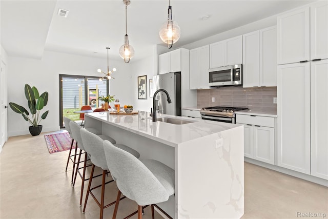 7614 Kipling Unit 15, Detroit, MI 48206 - kitchen featuring appliances with stainless steel finishes, a sink, backsplash, an island with sink, and white cabinets