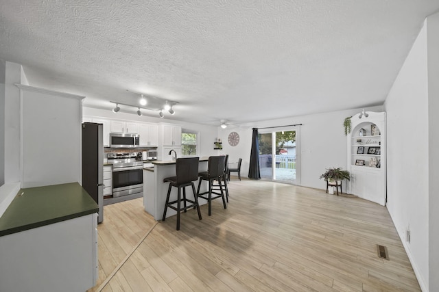 2837 Elmwood Dr, Adrian, MI 49221 - kitchen with appliances with stainless steel finishes, a breakfast bar, white cabinetry, light wood-type flooring, and an island with sink