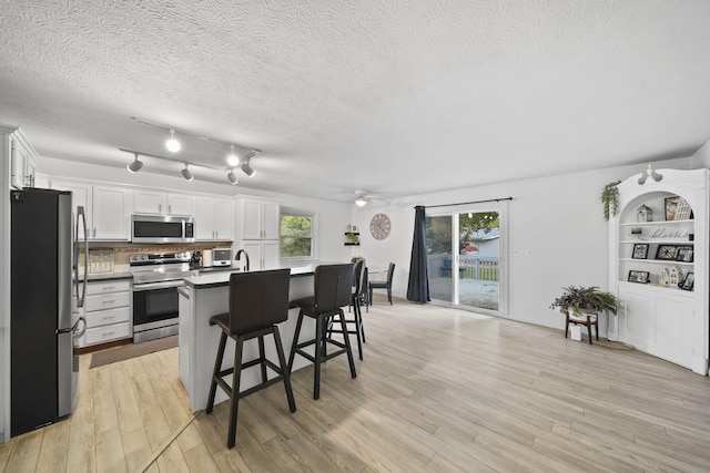 2837 Elmwood Dr, Adrian, MI 49221 - kitchen with appliances with stainless steel finishes, white cabinets, light wood-type flooring, a kitchen breakfast bar, and decorative backsplash