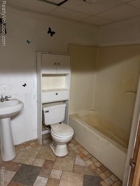 5736 Burnside Rd, North Branch, MI 48461 - bathroom with toilet, a paneled ceiling, washtub / shower combination, a sink, and stone finish floors