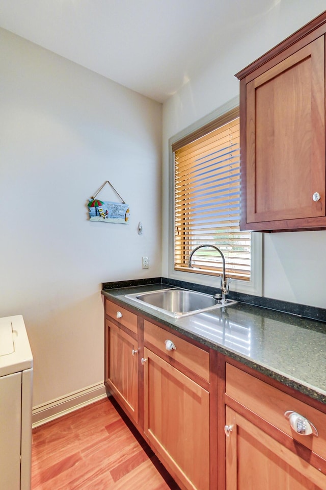 210 E Water St, New Buffalo, MI 49117 - kitchen featuring a sink, washer / clothes dryer, dark stone countertops, light wood-style floors, and brown cabinetry