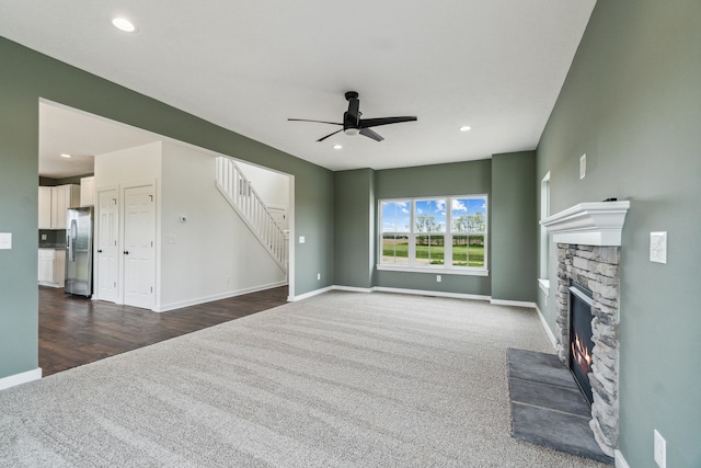 705 Montels Way, Charlotte, MI 48813 - unfurnished living room featuring a fireplace, a ceiling fan, dark colored carpet, baseboards, and stairway