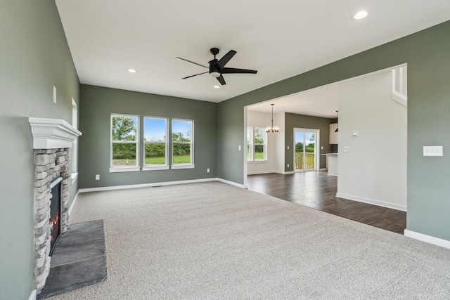 705 Montels Way, Charlotte, MI 48813 - unfurnished living room with dark carpet, ceiling fan, a stone fireplace, baseboards, and a chandelier