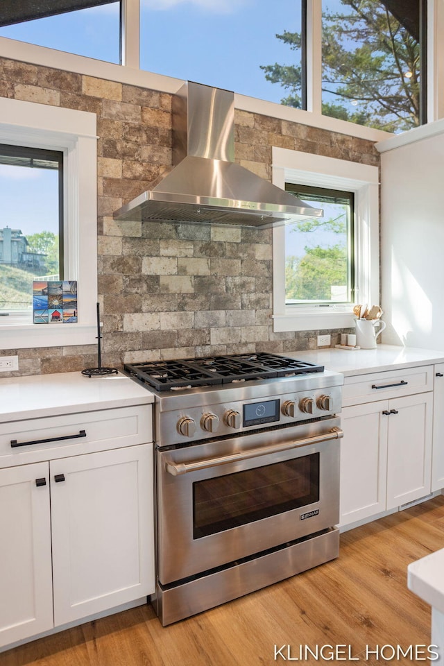127 Emmet St, Grand Haven, MI 49417 - kitchen with high end stainless steel range oven, wall chimney exhaust hood, tasteful backsplash, white cabinets, and light countertops