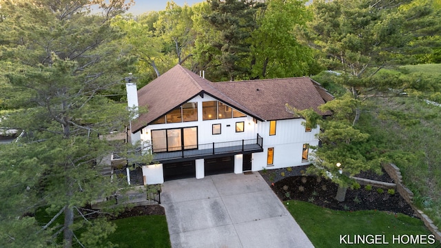 127 Emmet St, Grand Haven, MI 49417 - modern farmhouse with concrete driveway, an attached garage, a chimney, roof with shingles, and a forest view