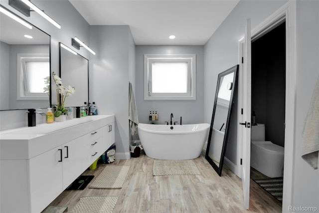 44200 Judd Rd, Belleville, MI 48111 - full bathroom featuring double vanity, a freestanding bath, toilet, wood finished floors, and baseboards