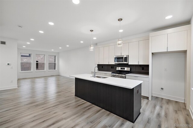2817 Summers Pl, Troy, MI 48084 - kitchen with stainless steel appliances, a sink, white cabinets, light wood-style flooring, and a kitchen island with sink