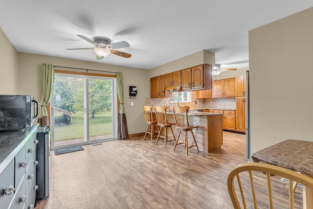 11245 Antcliff Rd, Brooklyn, MI 49230 - kitchen with a ceiling fan, a peninsula, a kitchen breakfast bar, light wood-style flooring, and decorative backsplash